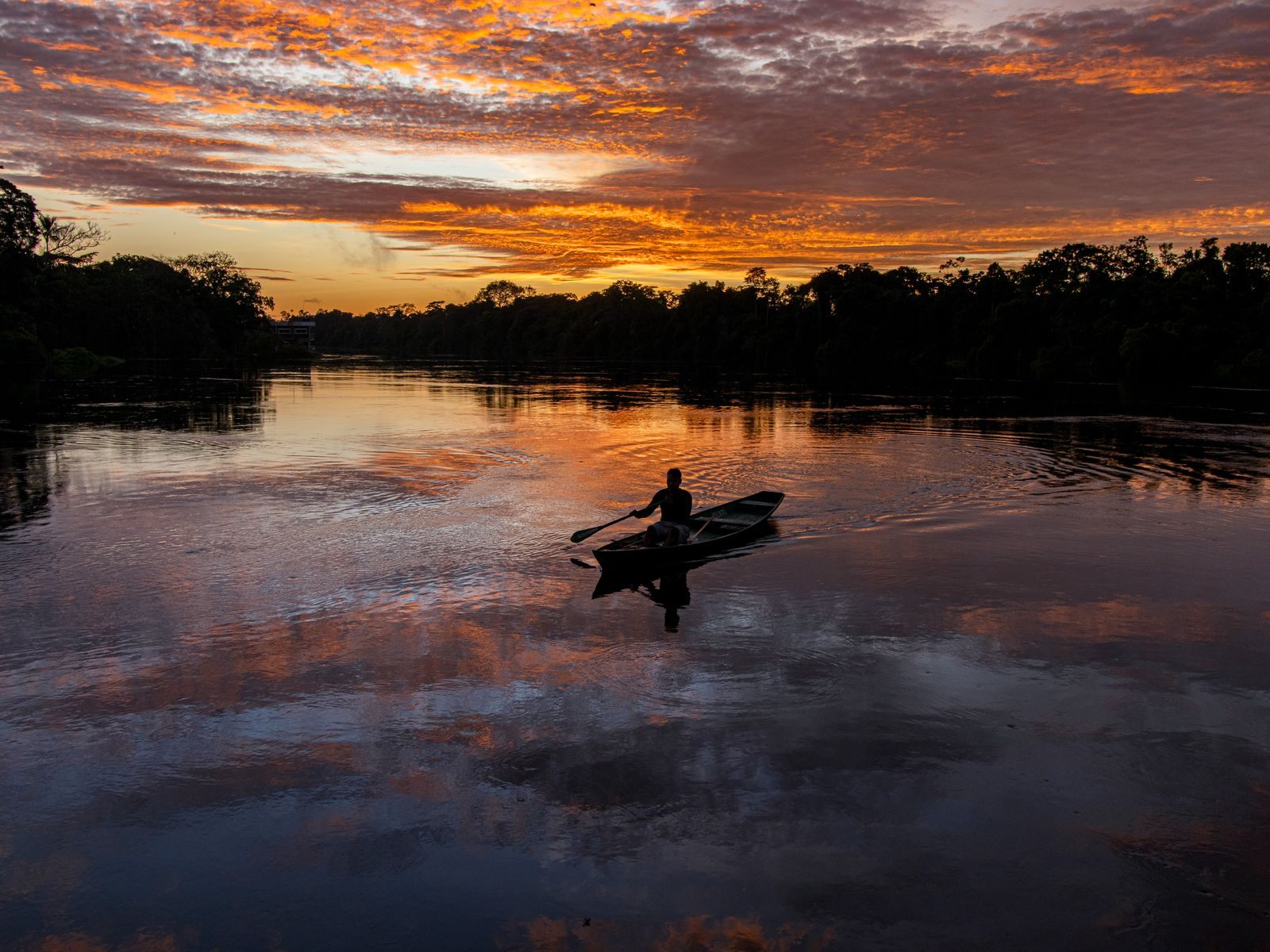 Fisherman rowing across the Amazon River in Brazil at sunset, a scene from South America river cruises